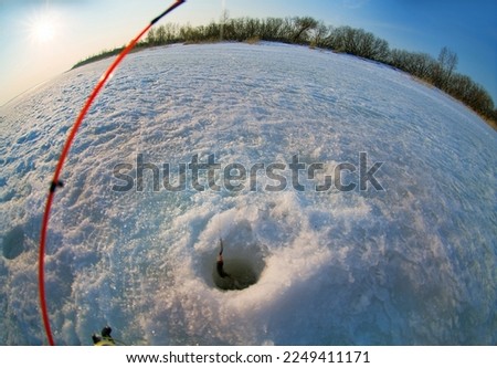 Ice recreational fishing. A picture of ruff fishing with a hole, winter rod, a panorama of the river and the forest shore. A fish-eye lens is used