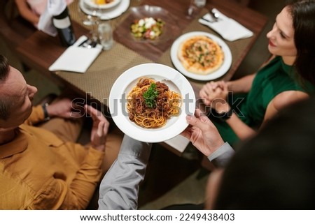 Restaurant waiter bringing plate with spaghetti bolognese to table Royalty-Free Stock Photo #2249438403