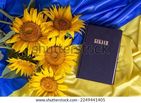 Bible (Holy Writ) and sunflowers on background of flag of Ukraine.
