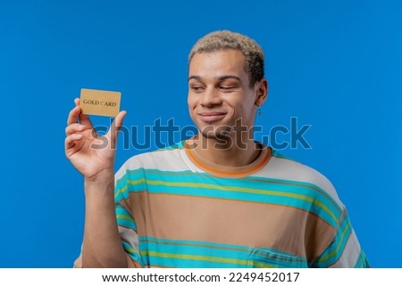 Successful handsome man showing unlimited gold credit card and look to camera blue studio background. High quality photo