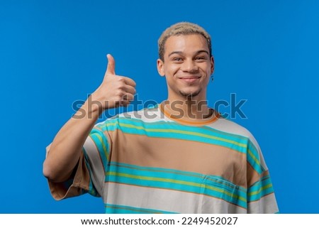 Positive man makes hand sign like, thumbs up gesture. Happy student guy in blue, correct perfect choice, great deal, studio background. . High quality photo