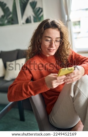 Young pretty woman holding smartphone using cellphone modern technology, looking at mobile, checking cell phone apps, texting typing messages, browsing internet for shopping sitting at home. Vertical Royalty-Free Stock Photo #2249452169