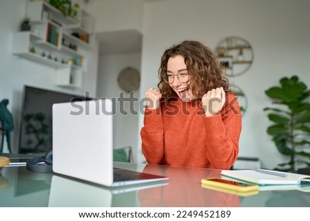Happy girl student winner looking at laptop receiving good news in email celebrating achievement success. Excited woman winning online, getting new approved job opportunity using computer at home. Royalty-Free Stock Photo #2249452189