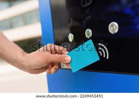 Woman pays for charging on a  Hypercharger or Supercharger with Nfc or Rfid card for electrical or hybrid PHEV automobiles charging, with copyspace for your individual text. Charge electromobility Royalty-Free Stock Photo #2249453451