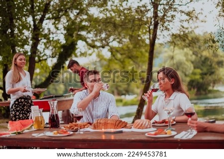 Group of happy friends having picnic french dinner party outdoor during summer holiday vacation near the river at beautiful nature