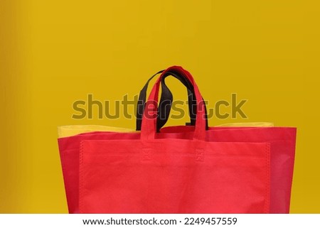 Non-Woven Grocery Shopping Bag with a yellow background. Collection of tote bags pink, green, orange, white, and blue polypropylene bags. pile of tote bags of non-woven fabric