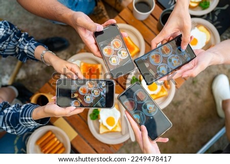 Group of Asian people using mobile phone photography meal during eating breakfast near the tent in the morning. Man and woman enjoy outdoor lifestyle travel nature camping on summer holiday vacation.