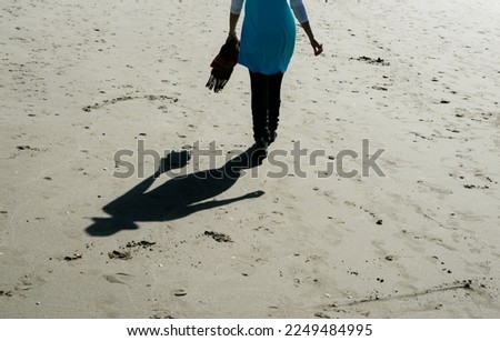 In silhouette person  and shadow from waist down walking away on beach.