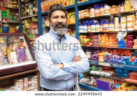 Portrait of happy mature Indian man standing at grocery shop or supermarket with cross arm. Royalty-Free Stock Photo #2249498645