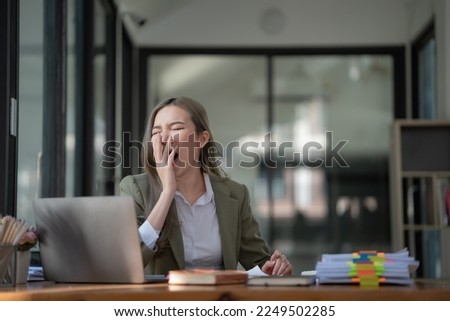 Young Asian businesswoman yawning while working with a laptop computer at the office, a woman in casual office lifestyle concept.