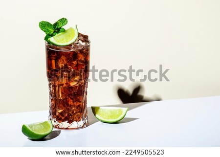 Whiskey cola cocktail with strong alcohol and ice, garnished with mint and lime in highball glass. Beige background, hard light Royalty-Free Stock Photo #2249505523