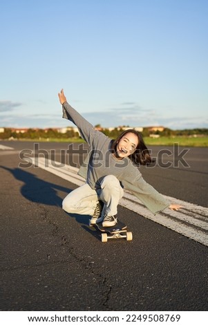 Carefree skater girl on her skateboard, riding longboard on an empty road, holding hands sideways and laughing. Royalty-Free Stock Photo #2249508769