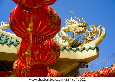 Chinese dragon statue on shrine roof. Selective focus on the dragon, and lantern foreground. Translation text "Flourish forever, money poured out of gold, forever filled". by Cheewasit Rakthammakit
