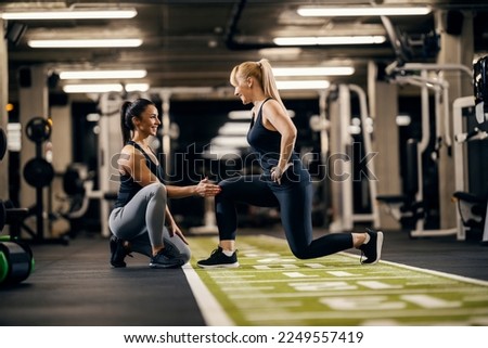 A female trainer is helping sportswoman to do exercises in a gym. Royalty-Free Stock Photo #2249557419