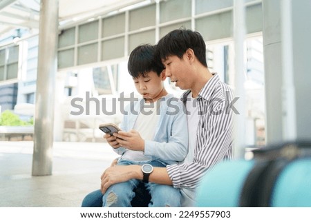 Happy cheerful Asian man and little boy traveling on the city railway station and using smartphone to take a selfie photography. Father and son using smartphone to take a photo or video call.