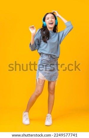 smiling asian cheerful young adult woman enjoy carefree music headphone freedom lifestyle,casual cloth asia woman hand gesture happiness photo studio shoot on yellow colour background full body Royalty-Free Stock Photo #2249577741