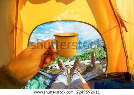 Cup of hot drink in the hand and wonderful view of mountain tops through the open entrance to the tent. The beauty of a romantic hike and camping accompanied by a dog.