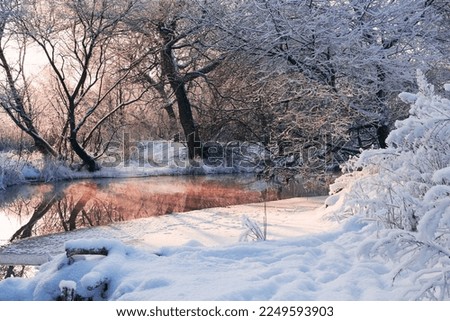 Tranquil winter river with snow covered trees. Christmas frosty landscape at sunrise or sunset with reflection in the water. Royalty-Free Stock Photo #2249593903