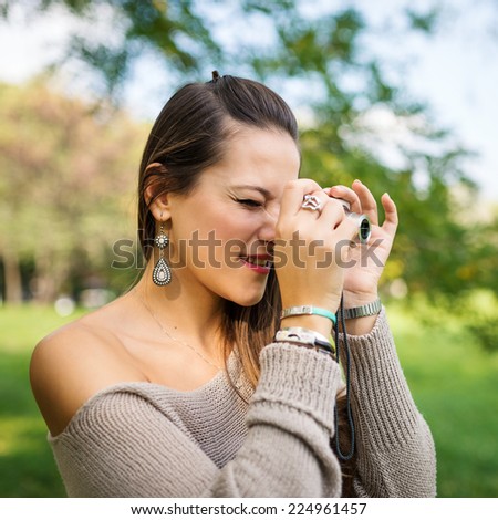 Portrait of young woman with compact camera outdoors in a park. 