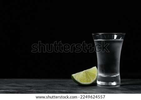 Shot of vodka with lime slice on grey table. Space for text