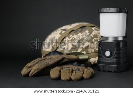 Tactical gloves, helmet and camping lantern on black background. Military training equipment