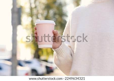 Woman holding pink takeaway cardboard cup on city street, closeup. Coffee to go