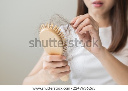 Serious asian young woman holding brush holding comb, hairbrush with fall black hair from scalp after brushing, looking on hand worry about balding. Health care, beauty treatment, hair loss problem. Royalty-Free Stock Photo #2249636265