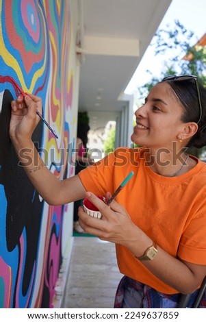 wall mural selective focus, beautiful woman in orange t-shirt paints the wall colorfully.Unfocused photo