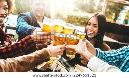 Happy multiracial friends cheering beer glasses at brewery pub garden - Group of young people enjoying dinner party eating and drinking at bar restaurant - Friendship and food and beverage concept Royalty-Free Stock Photo #2249651521