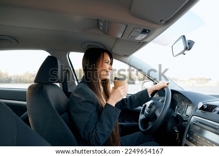 Beautiful woman holding steering wheel and coffee cup while driving a car, close-up view. Woman sipping a coffee while driving a car.