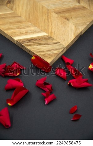 Red rose petals on a black background next to a wooden board for cooking.