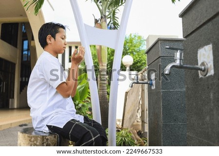 Muslim kid taking ablution for prayer, raise hand to pray before and after ablution   Royalty-Free Stock Photo #2249667533