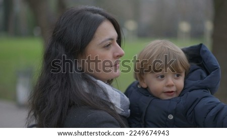 Mother walking outside holding baby toddler in arms, mom kissing son in cheek