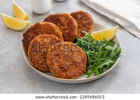 Tuna Patties or small fish cakes made with canned tuna, white beans, herbs and potato served on a plate with arugula salad and lemon wedges. Selective focus, gray concrete background. Horizontal. Royalty-Free Stock Photo #2249686053