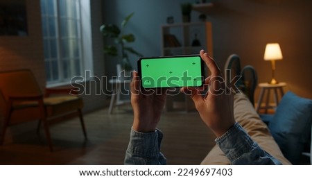 Close up shot of guy using his horizontal smart phone with mock up green screen at night, using various gestures while watching a video  Royalty-Free Stock Photo #2249697403