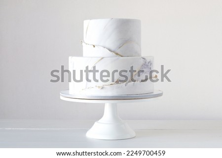 Cake with marble texture, decorated with gold confectionery sprinkles on a white background. Two-tiered white wedding cake. Royalty-Free Stock Photo #2249700459