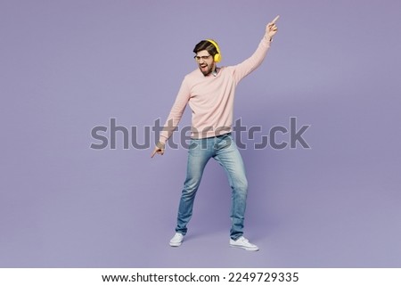 Full body young excited IT man he wear casual clothes pink sweater glasses headphones dance listen to music dance gesticulating hands isolated on plain pastel light purple background studio portrait