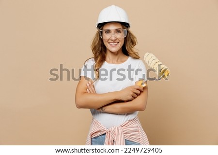 Young smiling happy employee laborer handyman woman in white t-shirt helmet hold roller paint walls isolated on plain beige background Instruments accessories for renovation room Repair home concept Royalty-Free Stock Photo #2249729405