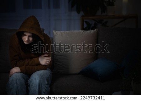 sad teenager girl sitting on couch indoor at night Royalty-Free Stock Photo #2249732411