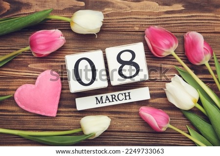 Flowers of tulips, pink felt heart and cube calendar on brown wooden background
