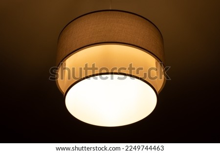 bright lamp burning in a round lampshade, lampshade lighting indoors on a dark background Royalty-Free Stock Photo #2249744463