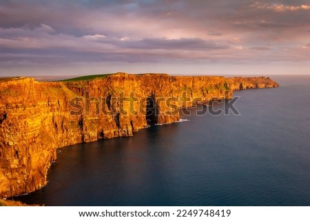 Cliffs of Moher, West of Ireland, glowing red at sunset, extending into the sea.