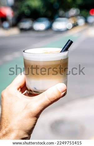  Cup of iced latte cappuccino coffee in hand on city street. Takeaway coffee drink