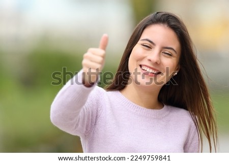 Front view portrait of a happy teen is gesturing thumbs up outdoors in a park