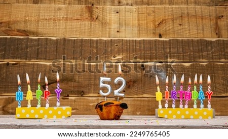 Muffin with a burning candle background for the anniversary on a beautiful wooden background. Postcard with letters of candles with congratulations for the holiday before the birthday. Copy space 52