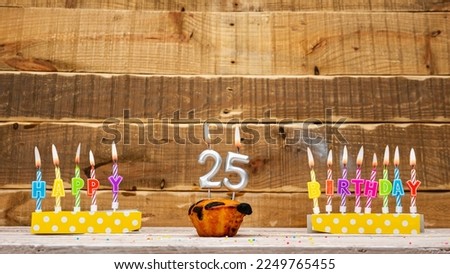 Muffin with a burning candle background for the anniversary on a beautiful wooden background. Postcard with letters of candles with congratulations for the holiday before the birthday. Copy space 25