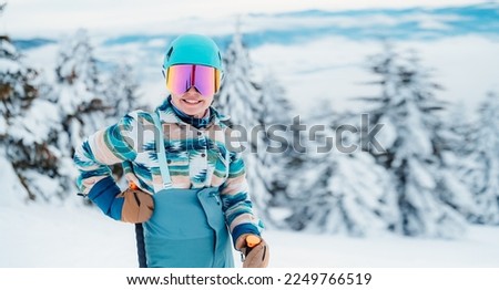 Woman in skiing clothes with helmet and ski googles on her head with ski sticks. Winter weather on the slopes. On top of a mountain and enjoying view. Alpine skier. Winter sport