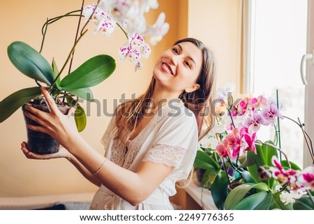 Smiling woman enjoys blooming white orchid with purple dots holding pot. Gardener takes care of home plants and flowers. Royalty-Free Stock Photo #2249776365