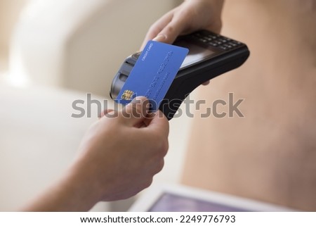 Hand of bank cardholder paying bill in cafe, applying blue credit card with chip at wireless payment terminal held by waitress, using electronic transaction banking technology. Clopped shot, close up Royalty-Free Stock Photo #2249776793