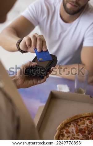 Male customer using credit card in cafe, paying for restaurant meal. Hand of waitress offering POS terminal to guest, holding gadget over table with pizza. Close up vertical shot Royalty-Free Stock Photo #2249776853